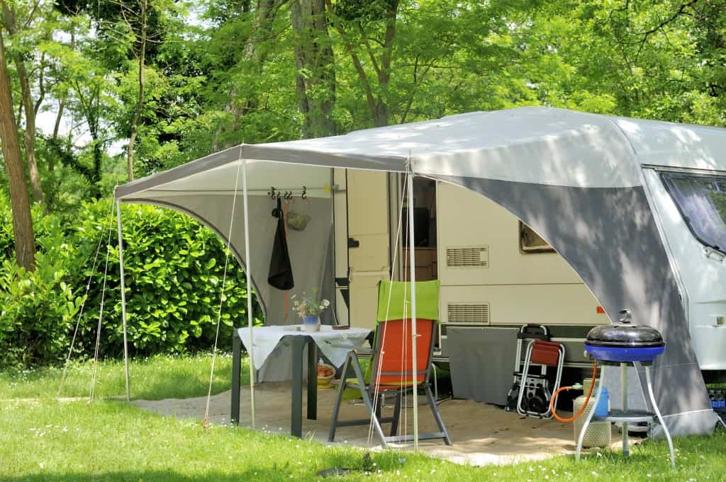 Campingvogn med utendørs sitteområde og grill i naturen.